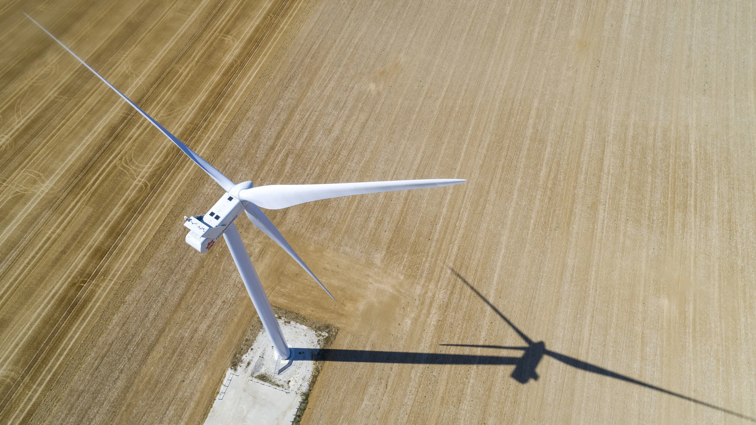 Vue aérienne d’une éolienne et de son ombre dans un champ.