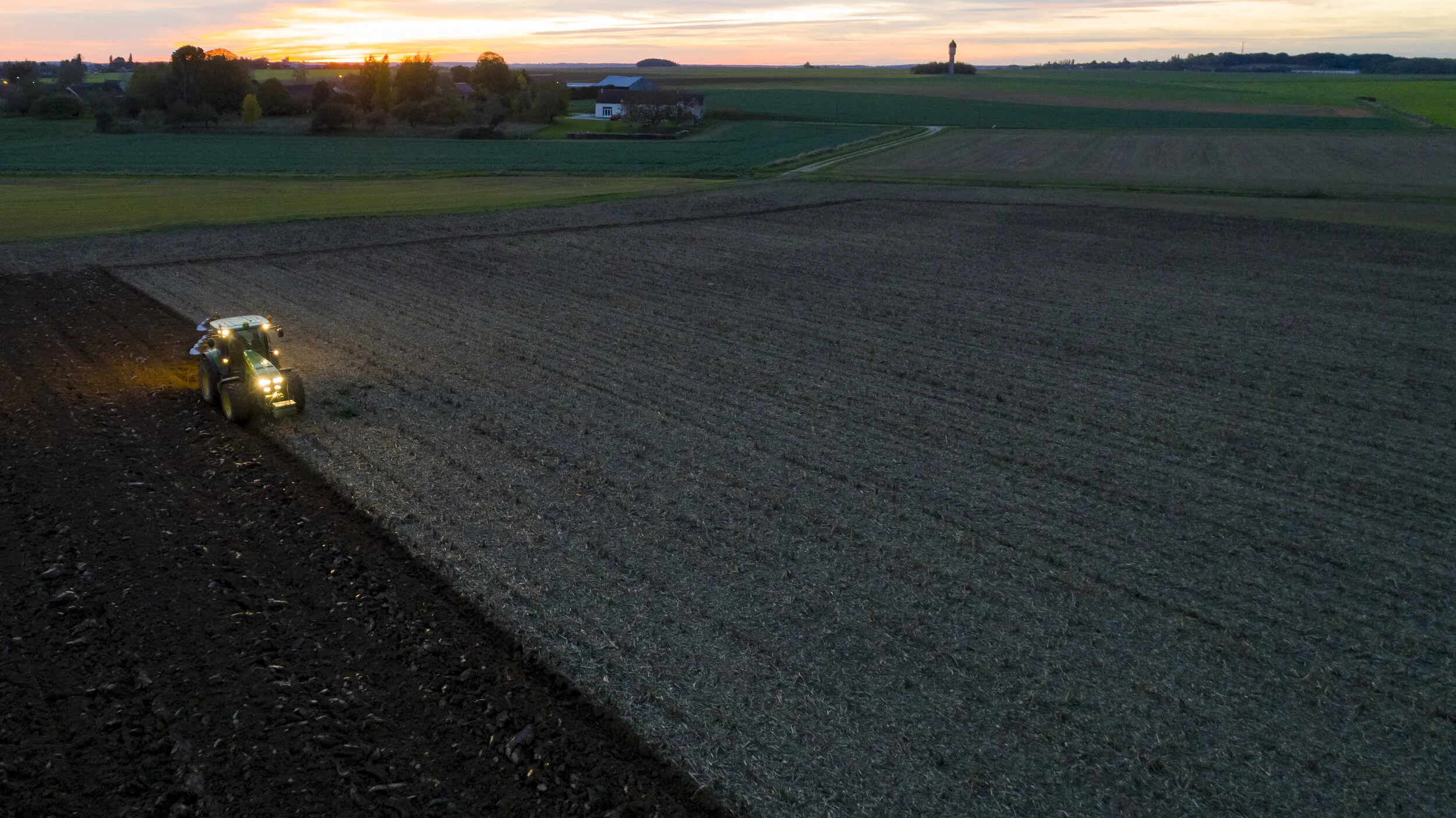 Tracteur dans un champ au coucher du soleil, vu depuis les airs.