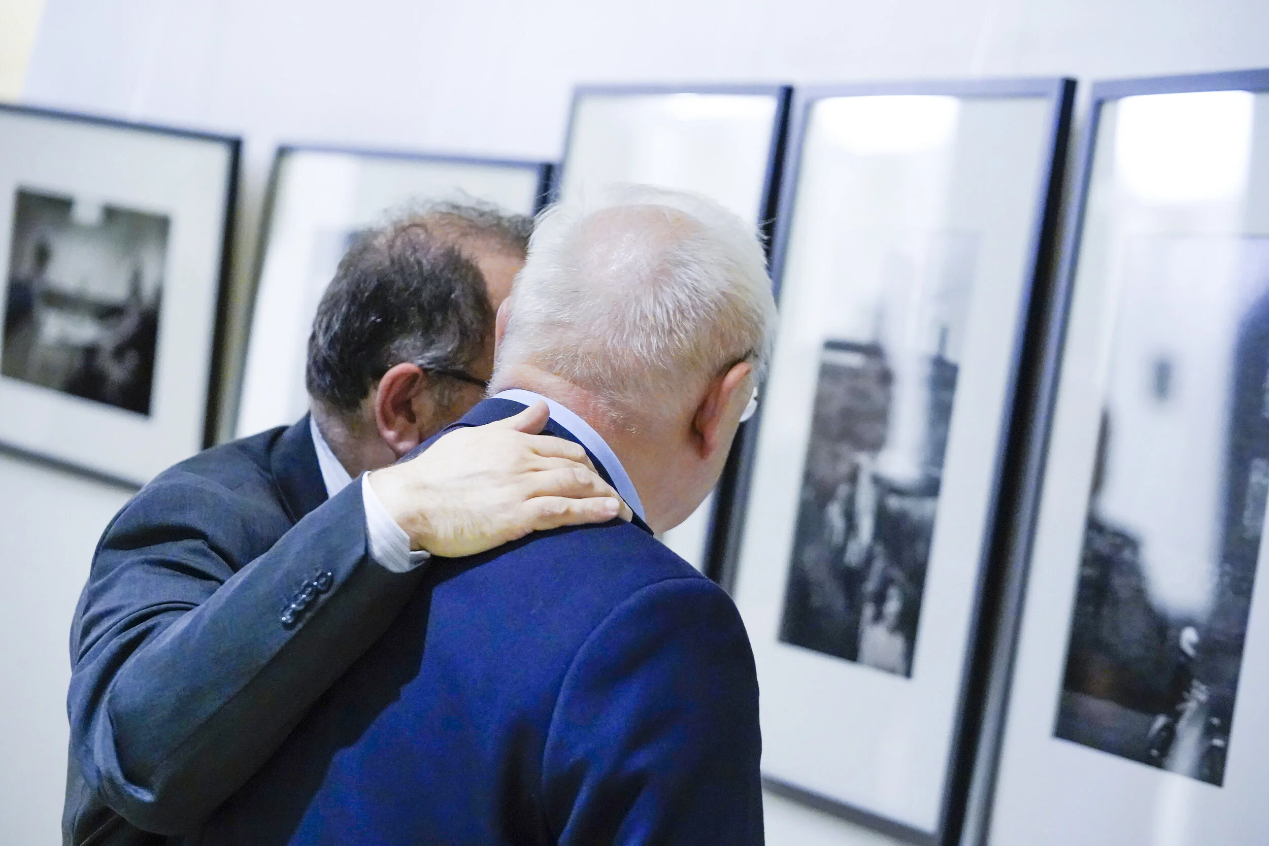 Deux hommes en costume devant des photographies encadrées, l’un posant la main sur l’épaule de l’autre, lors de l’inauguration d’une exposition au Comité économique et social européen.