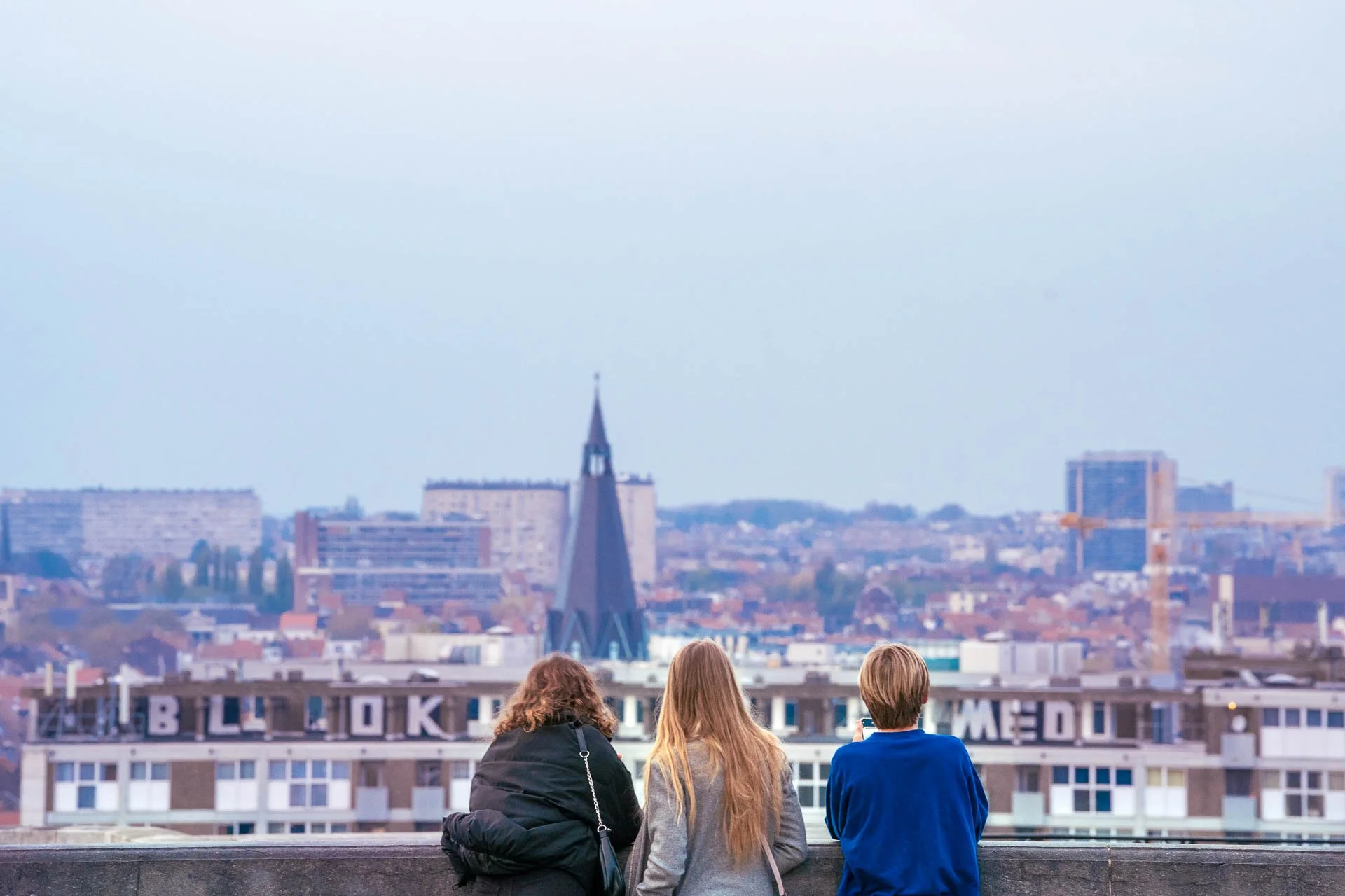 Des visiteurs contemplent Bruxelles depuis un point de vue en hauteur, avec les toits et une flèche à l’horizon.