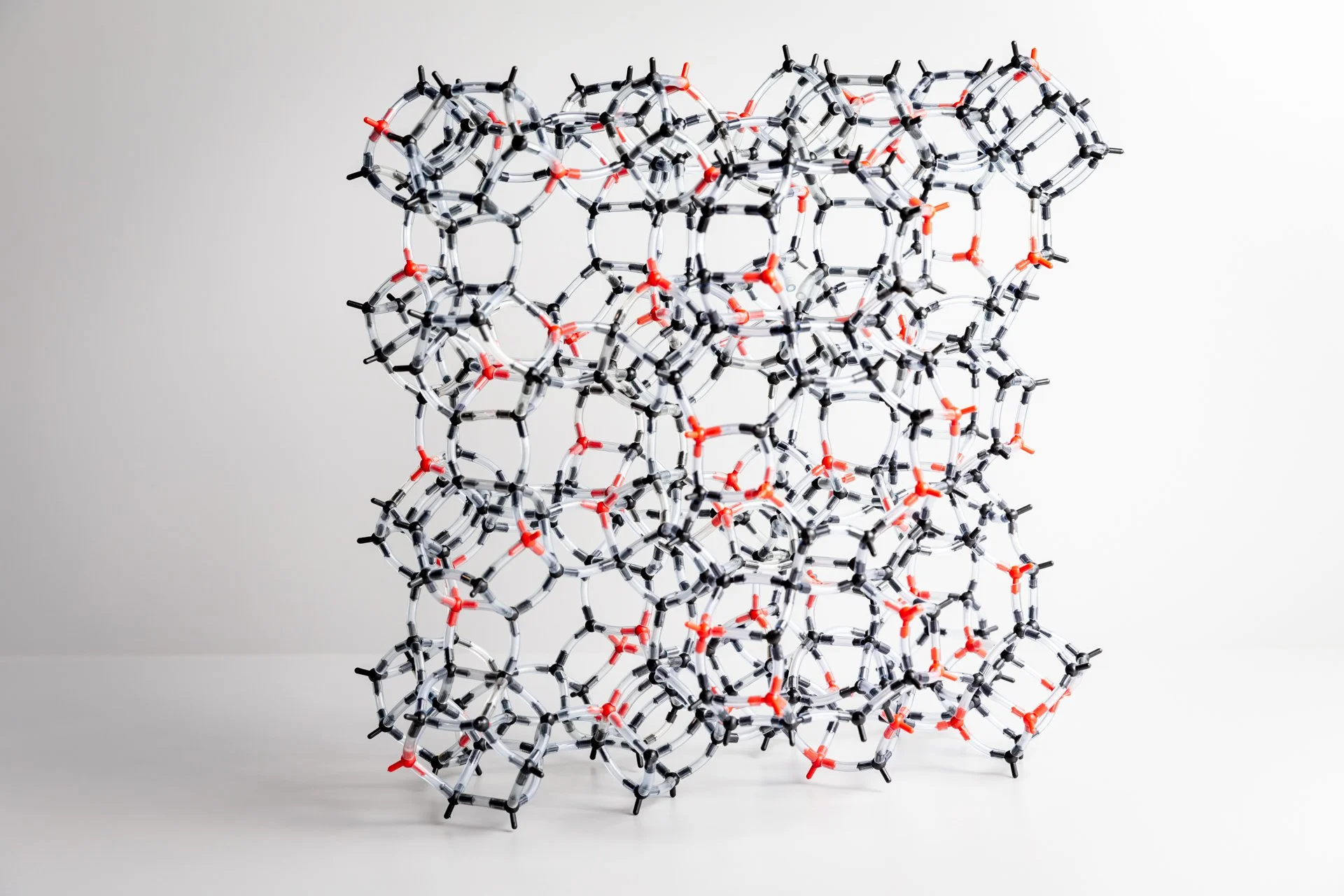 Modèle moléculaire géométrique composé de bâtonnets et de connecteurs noirs et rouges, photographié sur un fond blanc.