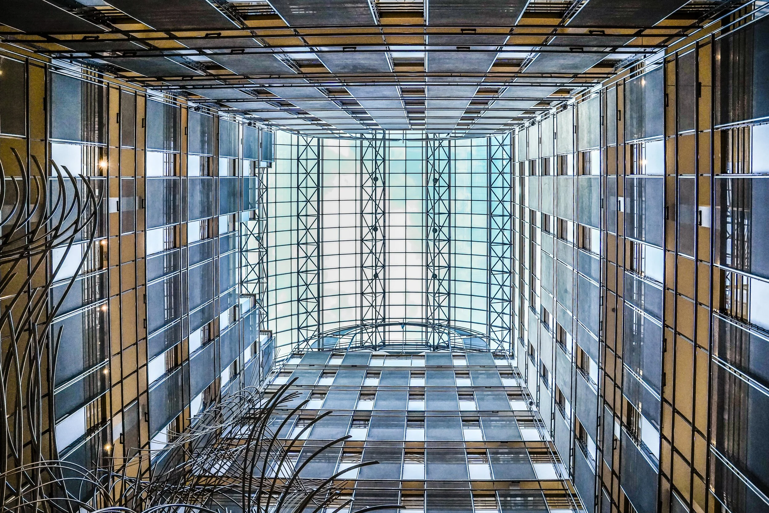 Vue en contre-plongée de l’atrium du bâtiment PHS du Parlement européen à Bruxelles, avec ses façades intérieures géométriques et sa verrière.