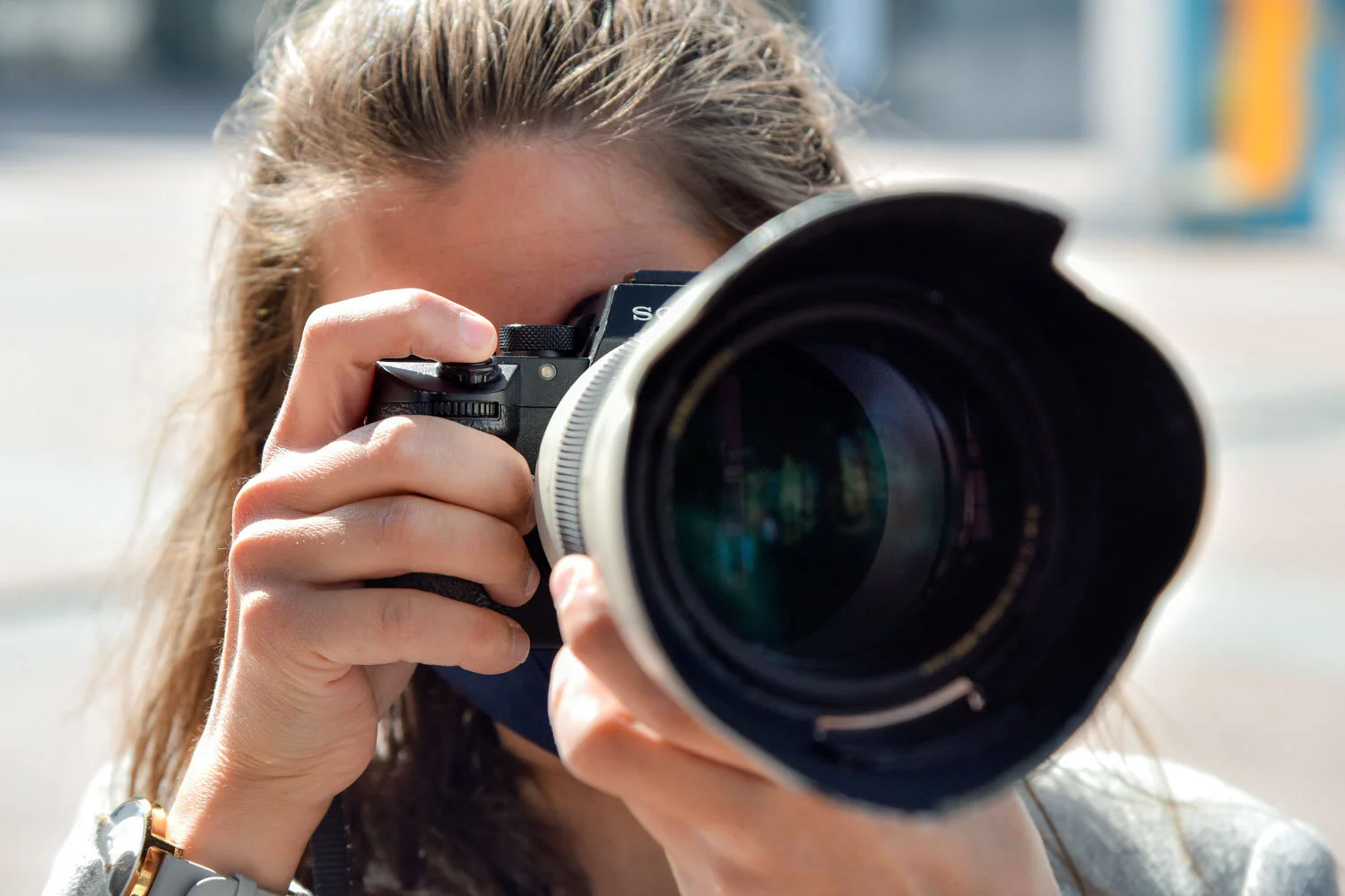 Gros plan sur une photographe regardant dans le viseur de son appareil, l’objectif dirigé vers le spectateur.