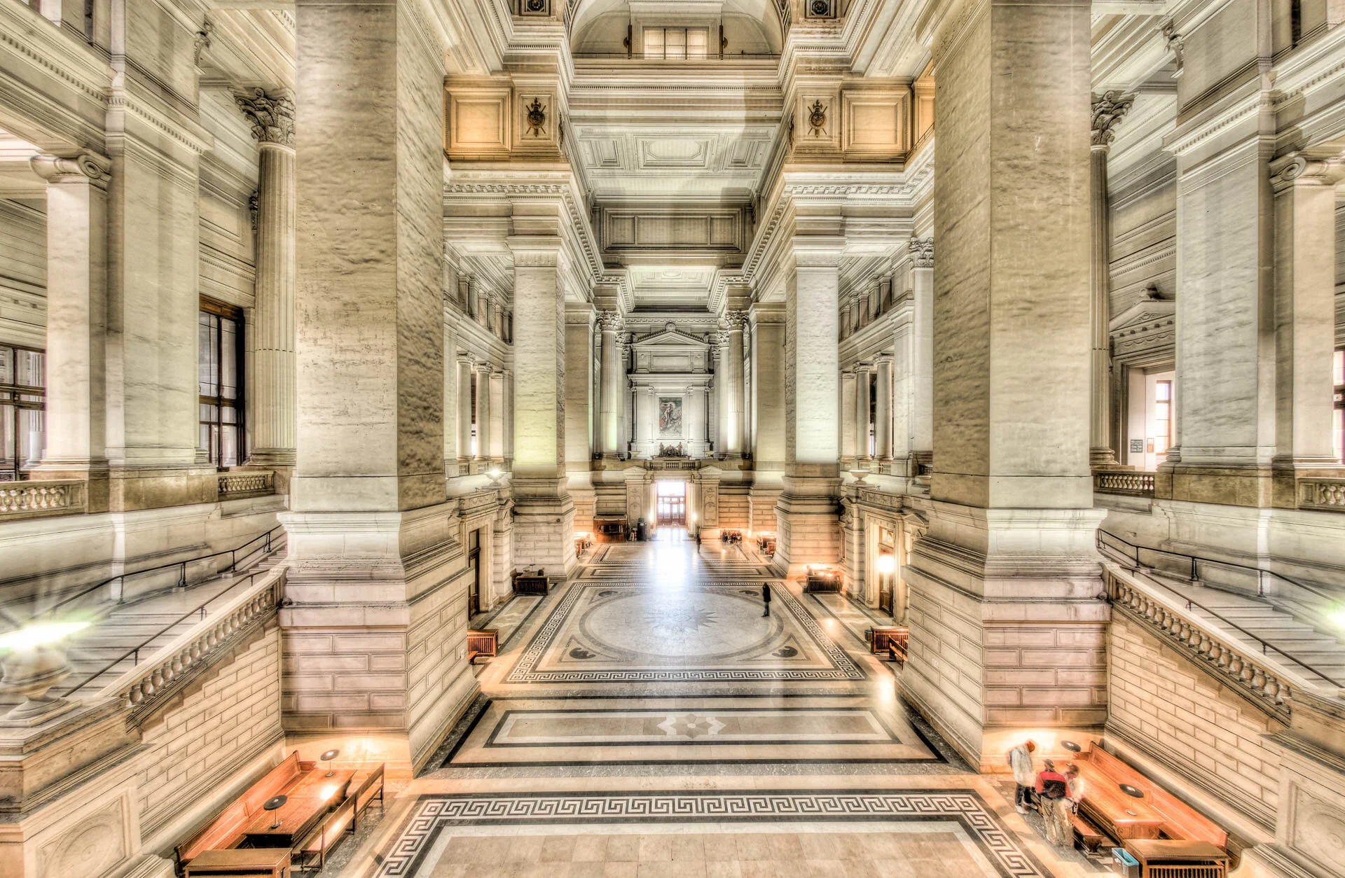 Hall monumental du Palais de Justice de Bruxelles, avec de hautes colonnes en pierre et un sol à motifs géométriques.