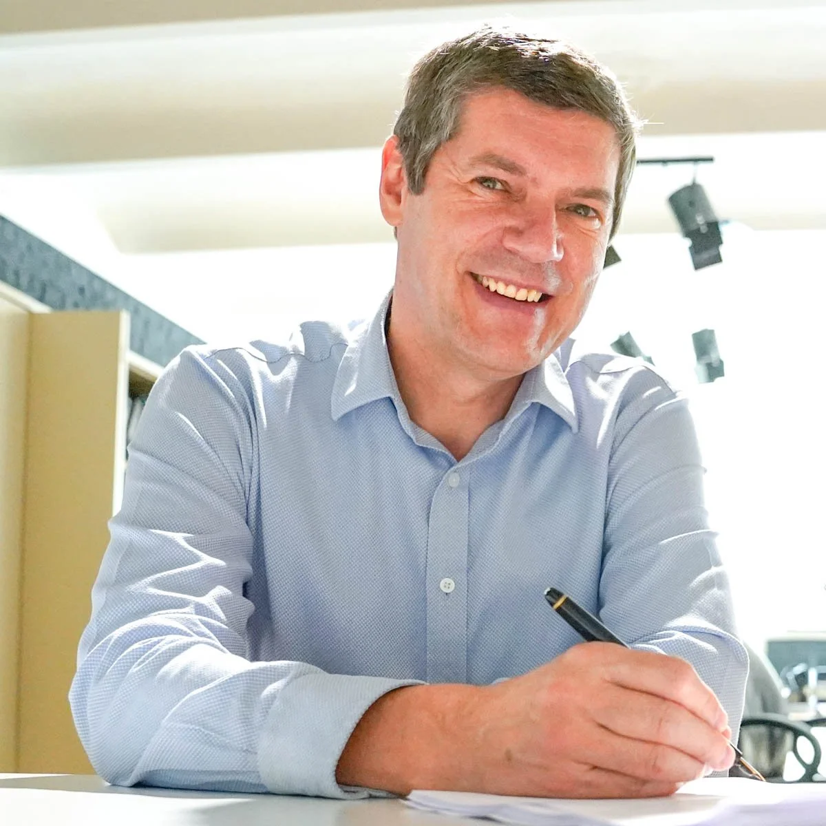 Paul Marnef, fondateur d’ISOWAY, souriant en chemise bleu clair, assis à une table avec un stylo à la main.