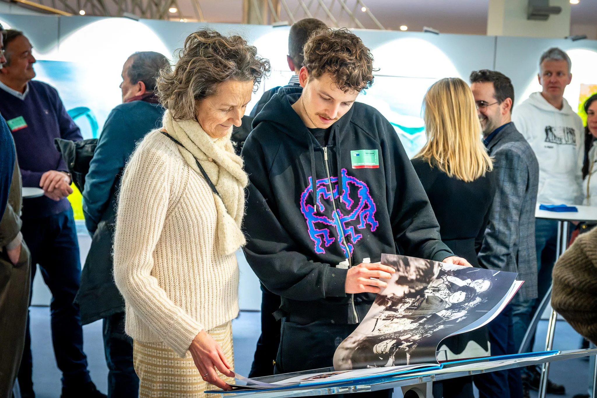 un event à Bruxelles.Un homme et une femme regardent une photo en noir et blanc dans un environnement avec plusieurs personnes en arrière-plan.