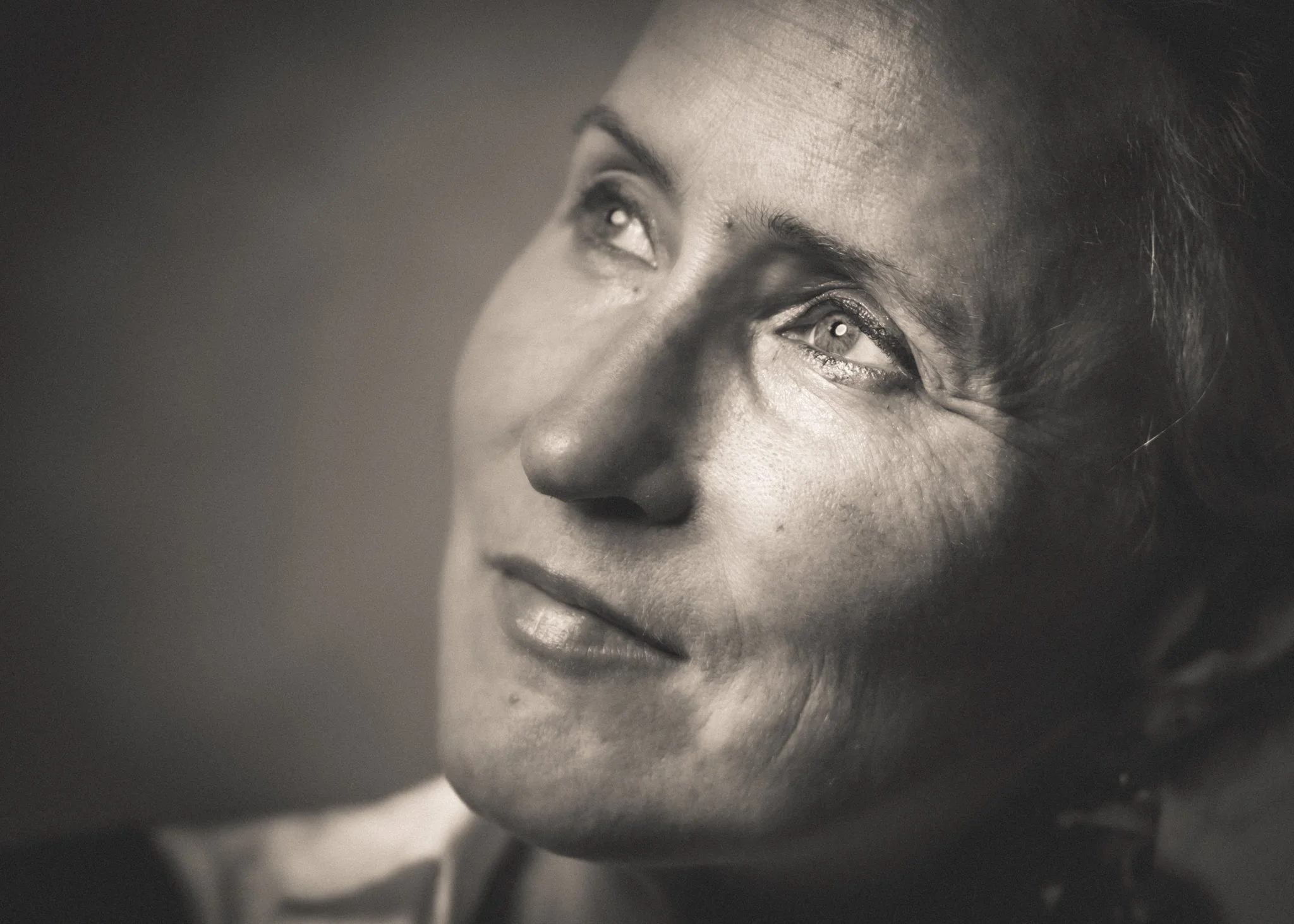 Portrait en noir et blanc de Sarah Debeuckelaer, le visage éclairé de côté et le regard dirigé vers le haut.