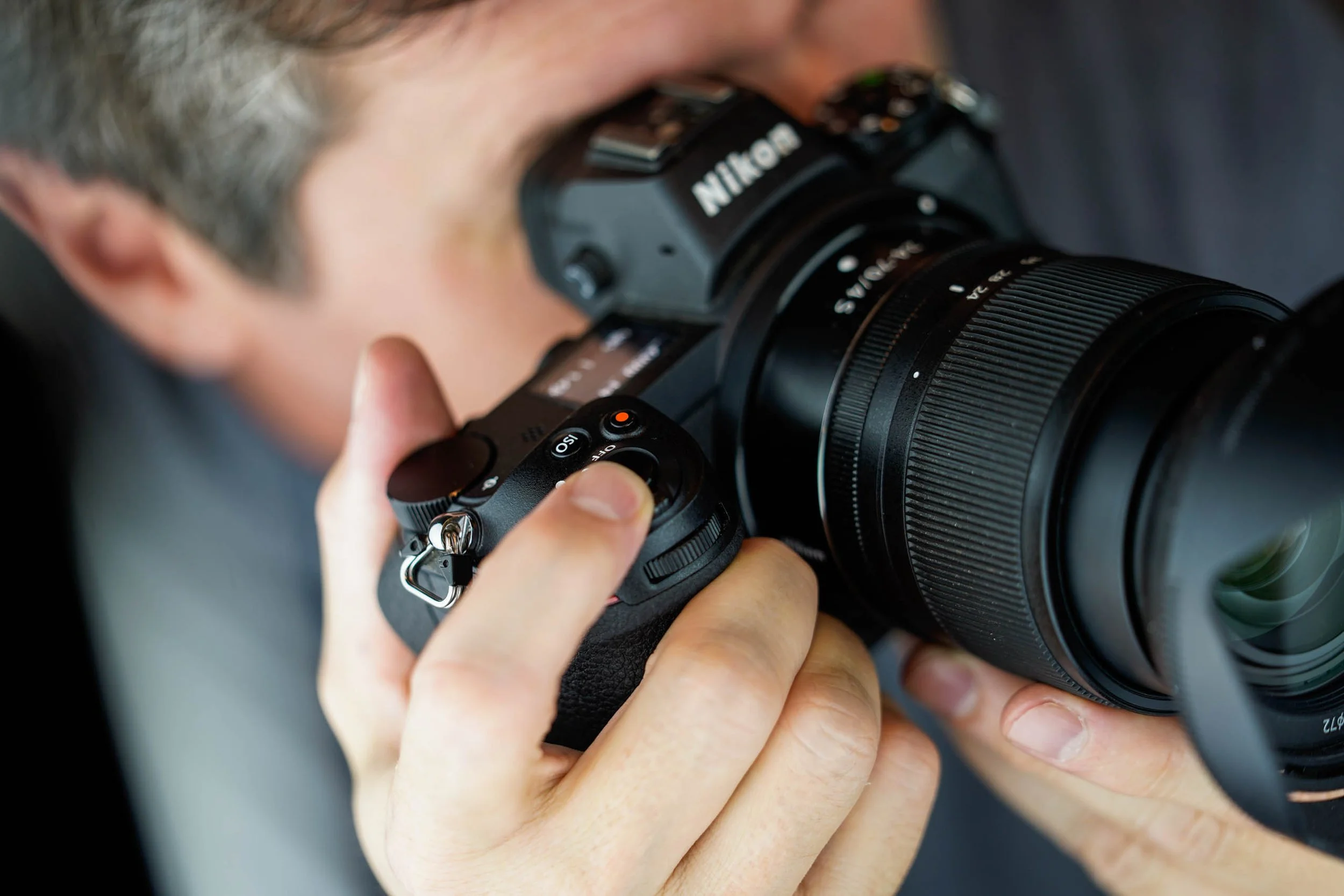 Gros plan sur un photographe regardant dans le viseur d’un appareil Nikon équipé d’un téléobjectif.