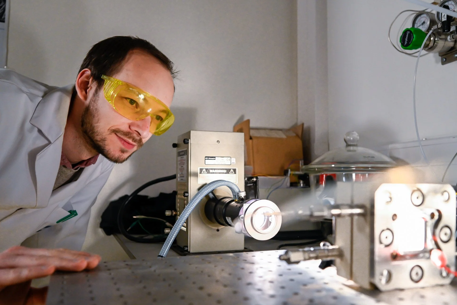 Un homme en blouse blanche et lunettes de protection jaunes observe un appareil de laboratoire.