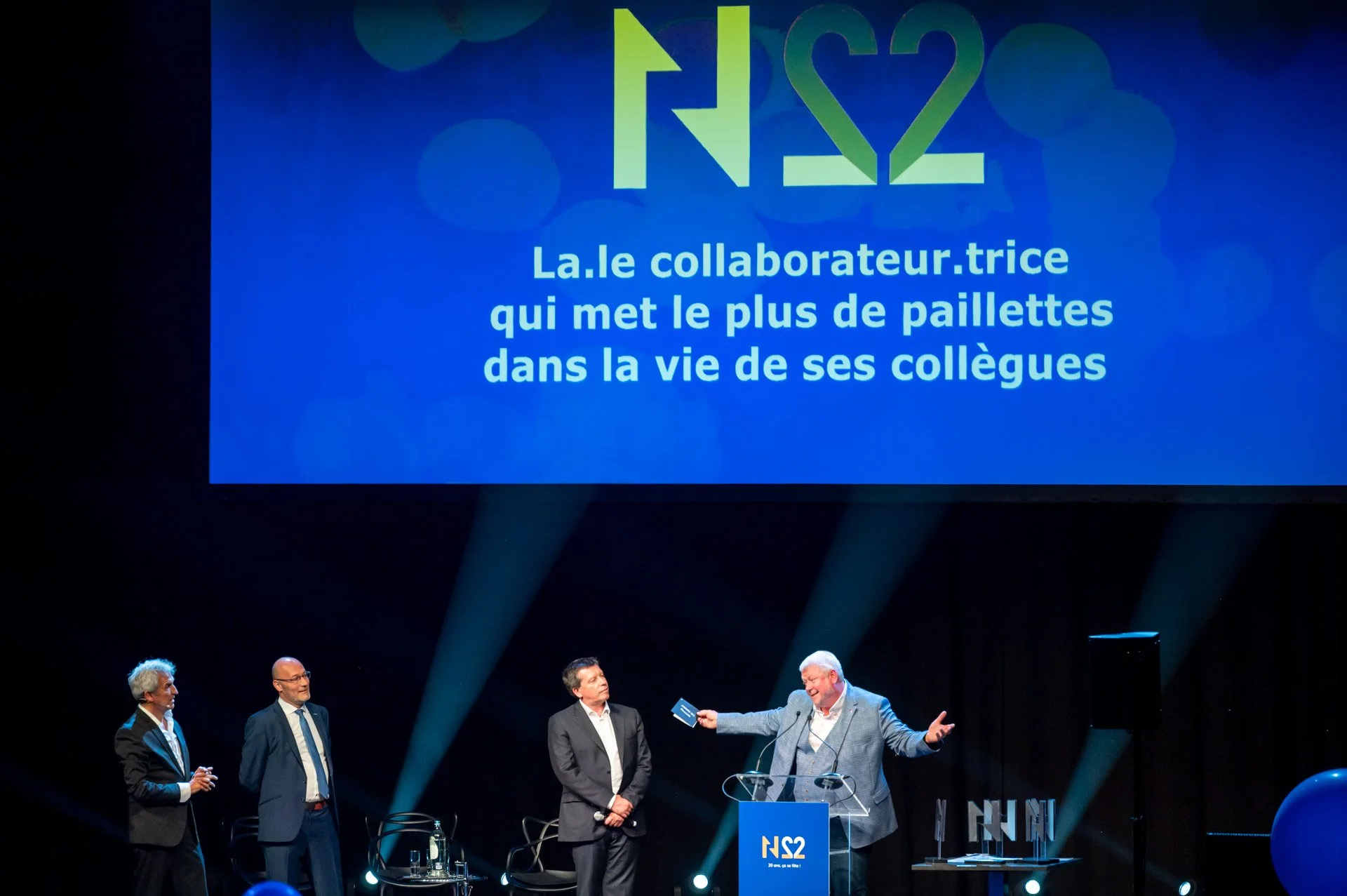 Quatre personnes sur scène lors d’une remise de prix, devant un écran annonçant la catégorie du collaborateur ou de la collaboratrice qui met des paillettes dans la vie de ses collègues.