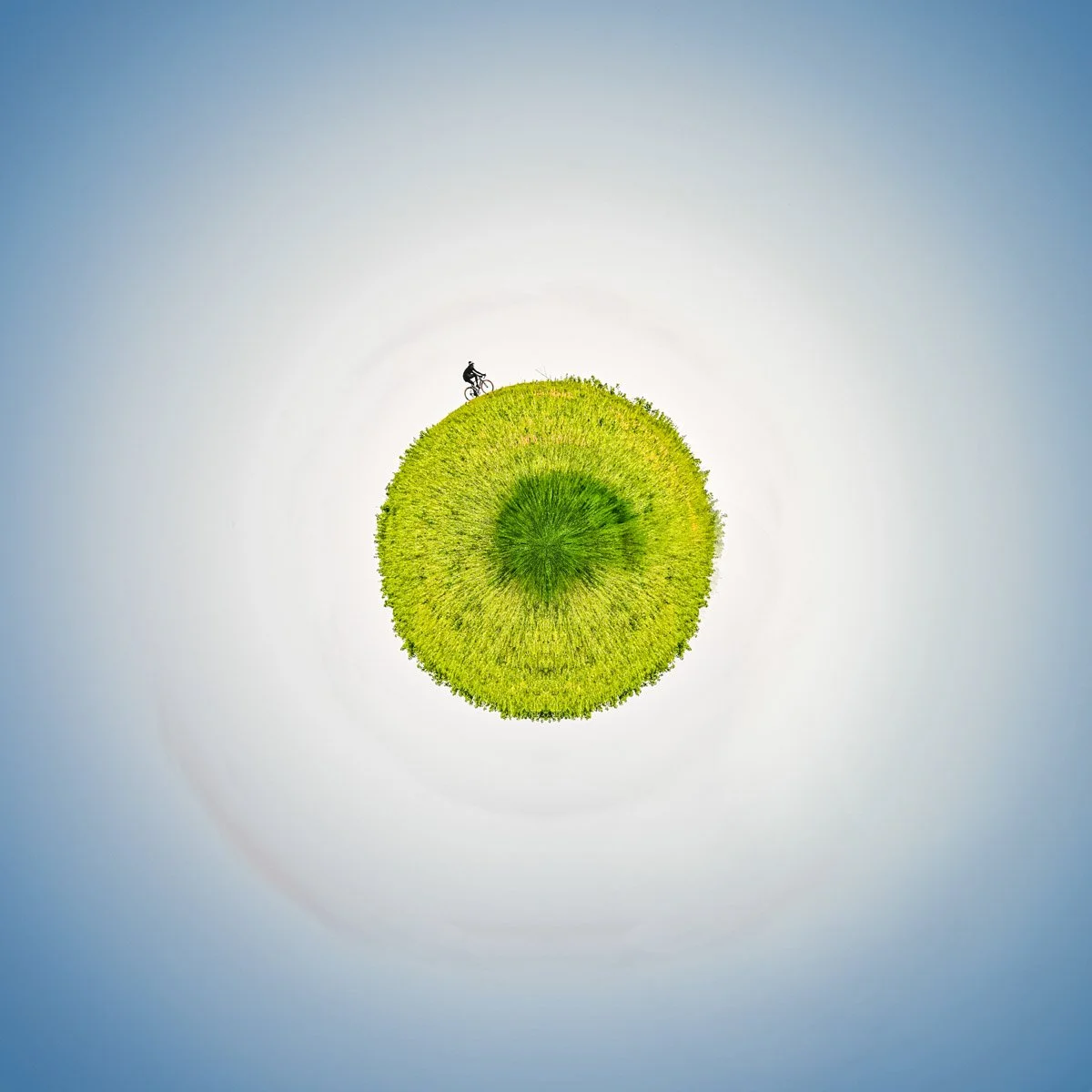 Une petite planète de verdure entourée d’un vaste halo blanc et d’un ciel bleu, avec une silhouette sur son pourtour.