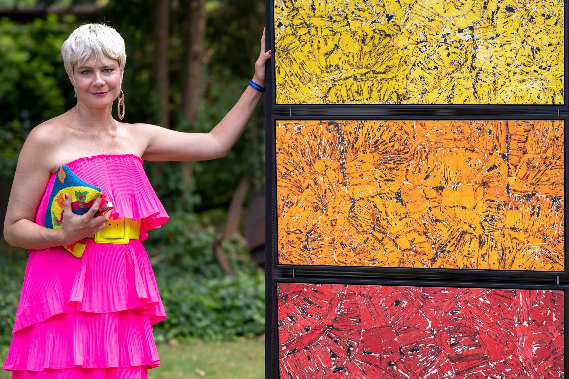 Stefanie Gasser, en robe rose, pose près de panneaux peints en jaune, orange et rouge lors de la Summer Party à la Villa Empain.