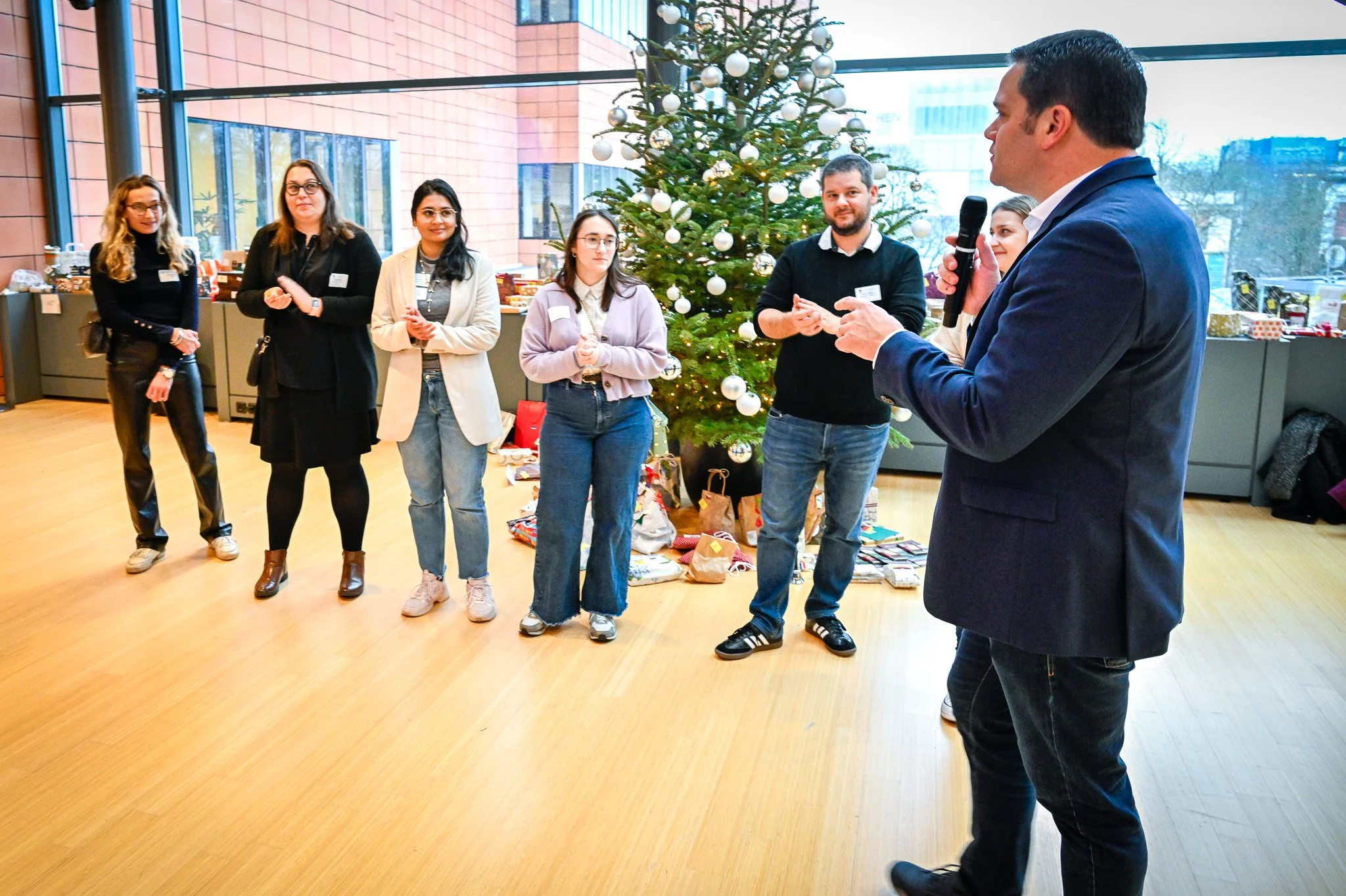 un événement organisé dans les locaux du Comité des Régions à Bruxelles. Groupe de personnes debout à l'intérieur, près d'un sapin de Noël décoré, un homme tenant un microphone.