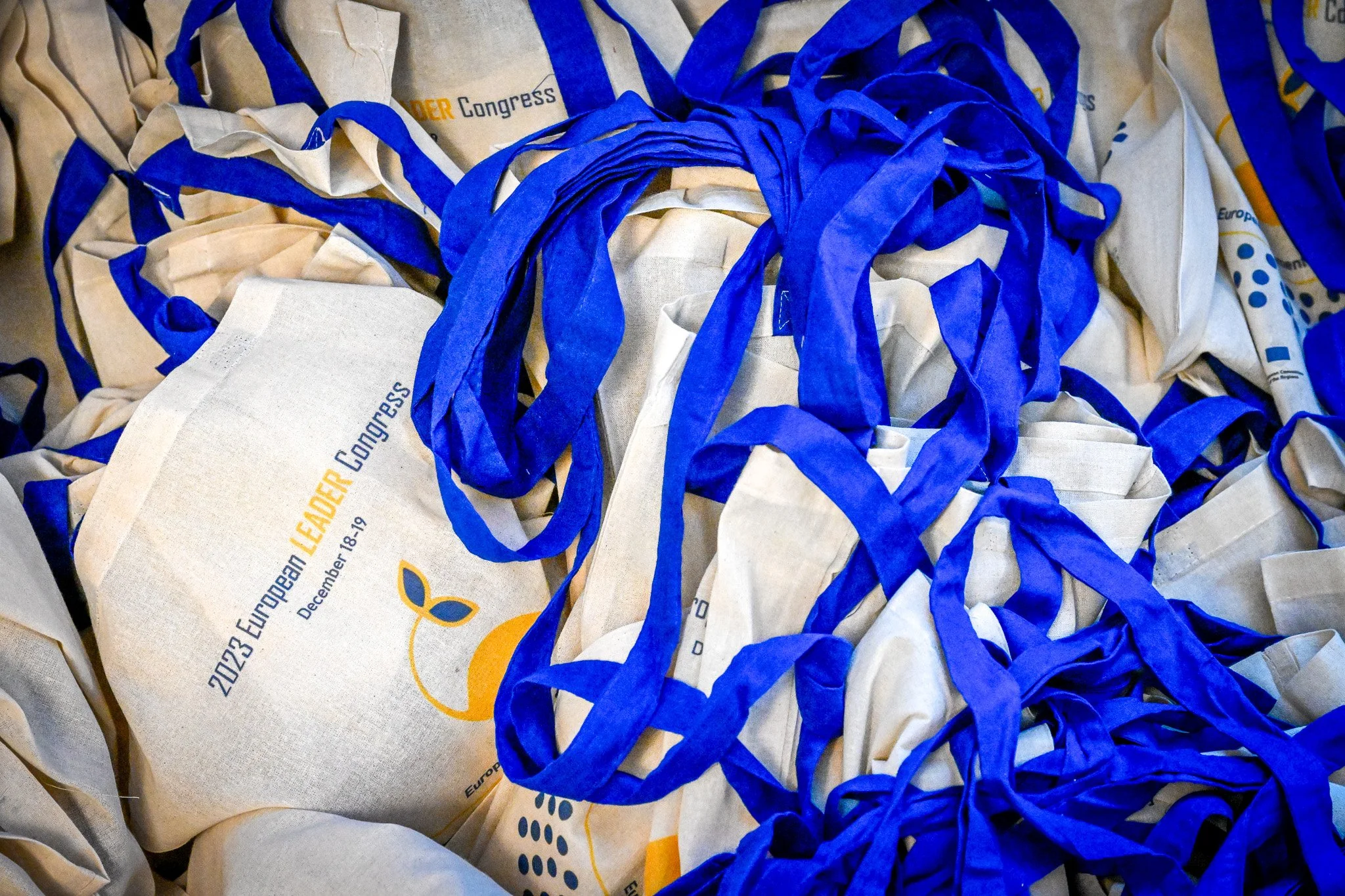 Des sacs en toile avec des poignées bleues portant l'inscription "2023 European LEADER Congress".