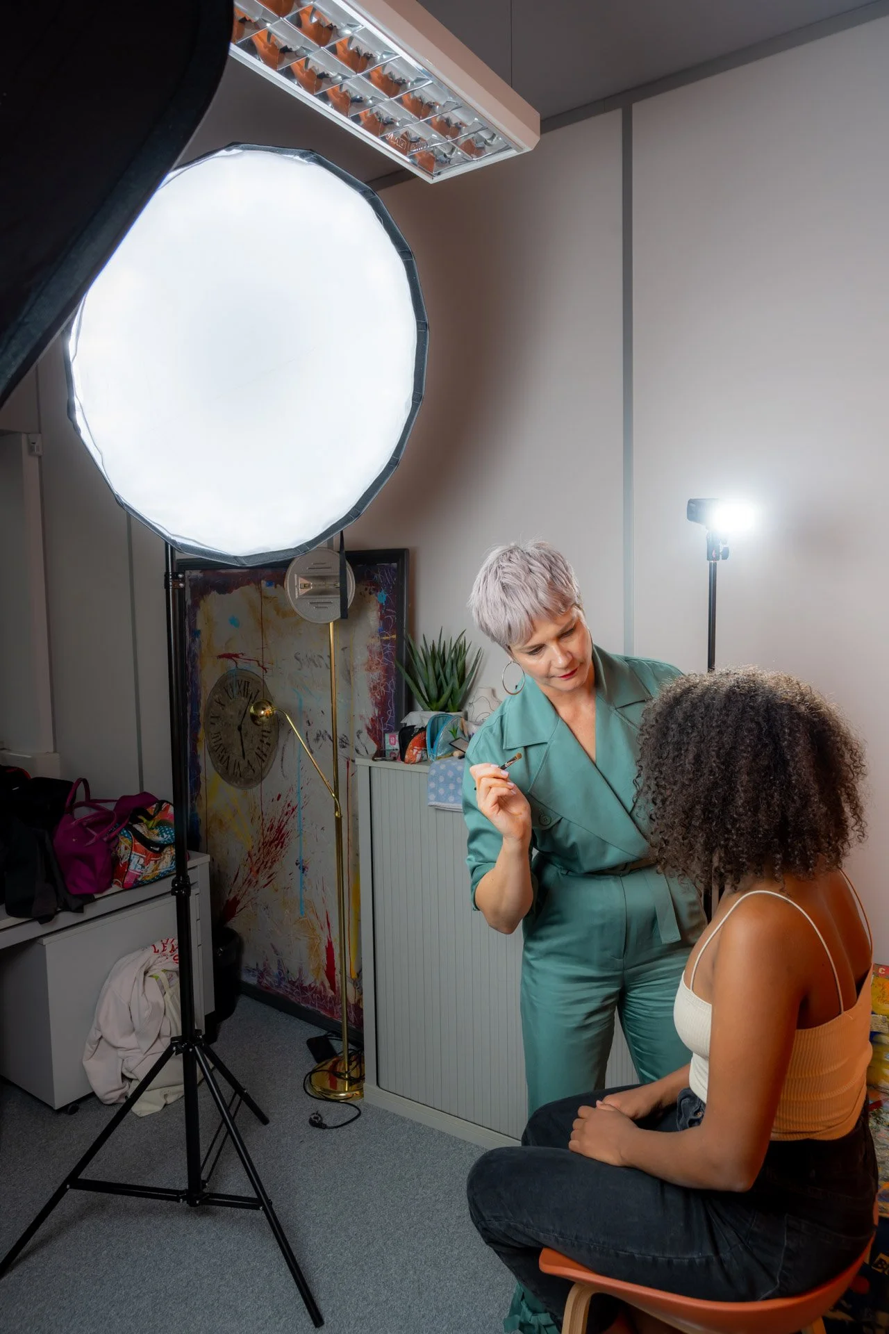 Une maquilleuse, Stefanie Gasser, prépare une femme assise dans un studio photo, près d’une grande boîte à lumière.
