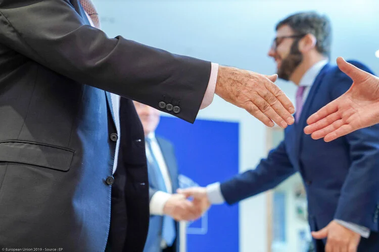 Des participants en costume se saluent lors d’une rencontre professionnelle, avec des mains tendues au premier plan.