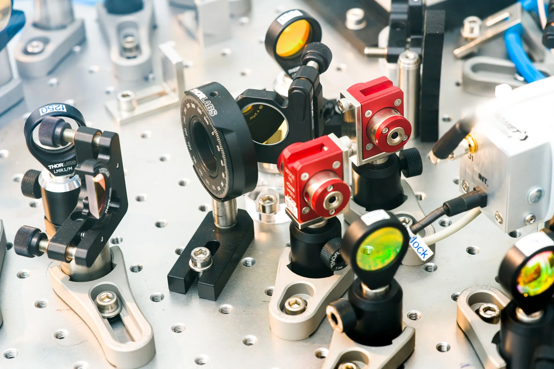Détail de composants optiques et de montages mécaniques fixés sur une table optique perforée.