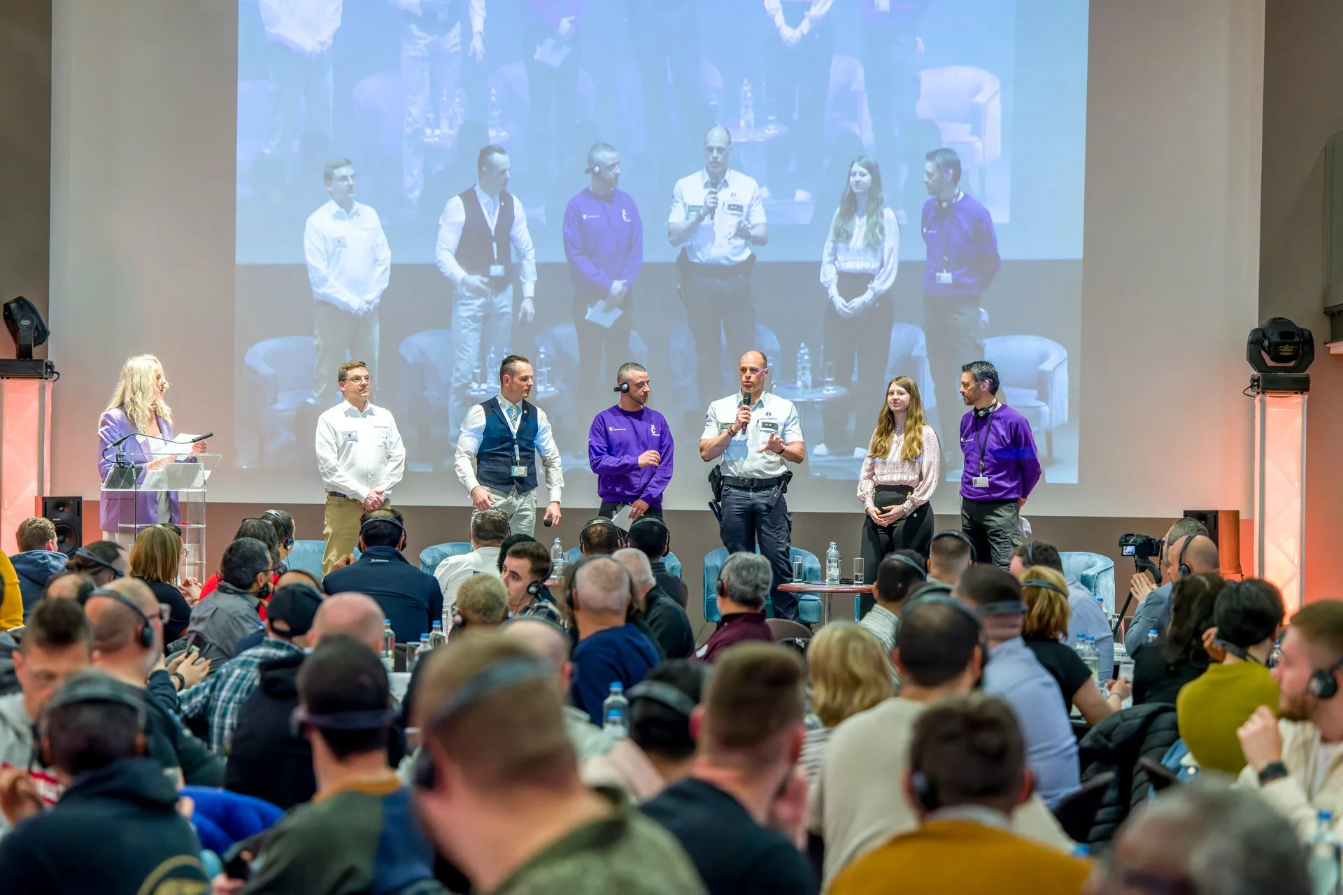 Des intervenants sur scène face au public d’une conférence, avec leur image projetée sur grand écran.