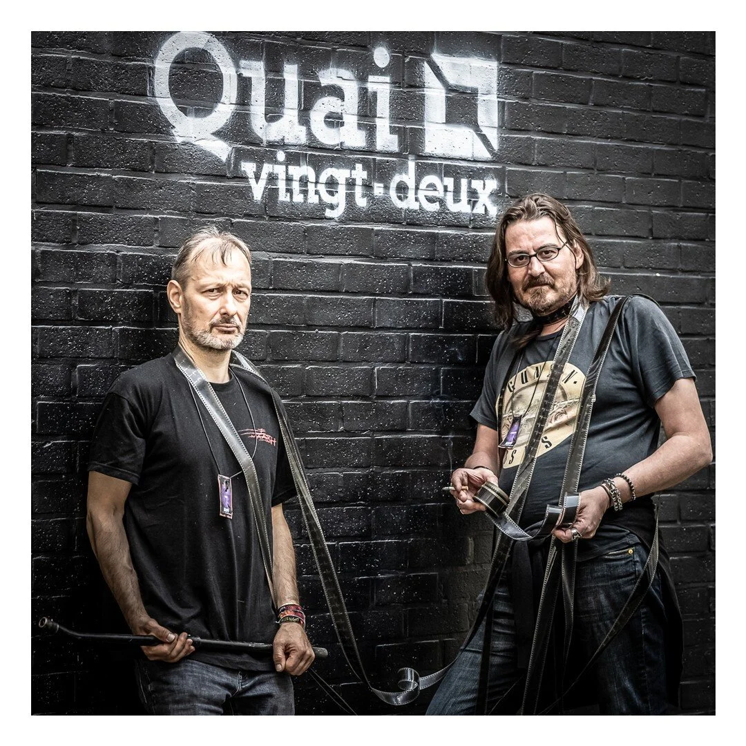 Deux hommes posent devant un mur de briques portant l’inscription Quai vingt-deux.