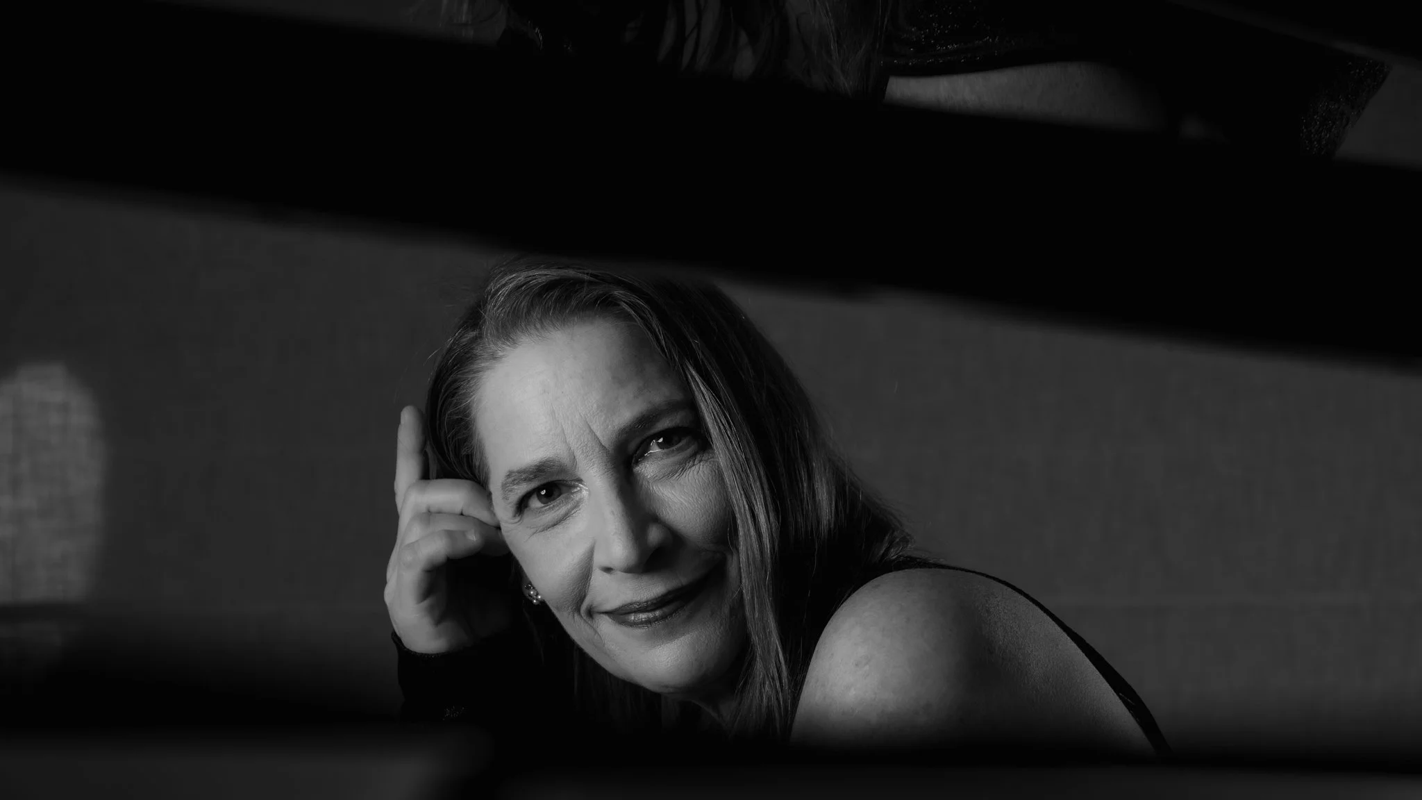 en noir et blanc de Nadia Weintraub souriante regardant vers l'objectif, avec un bras posé sur un coussin ou une banquette, prise de vue en contre-plongée.