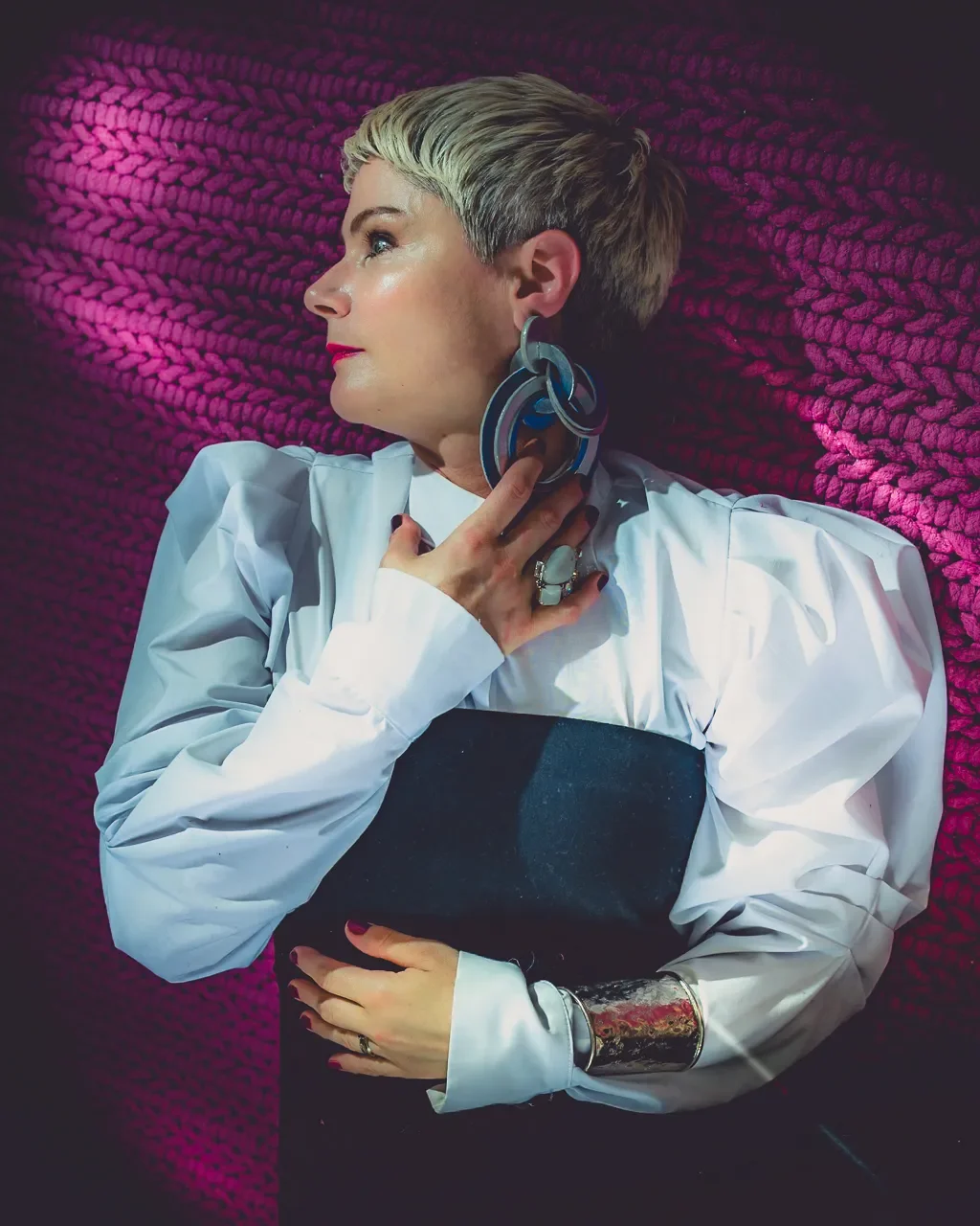 Portrait de profil d’une femme, Stefanie Gasser, aux cheveux courts, en blouse blanche et tenue sombre, devant un fond rose texturé.