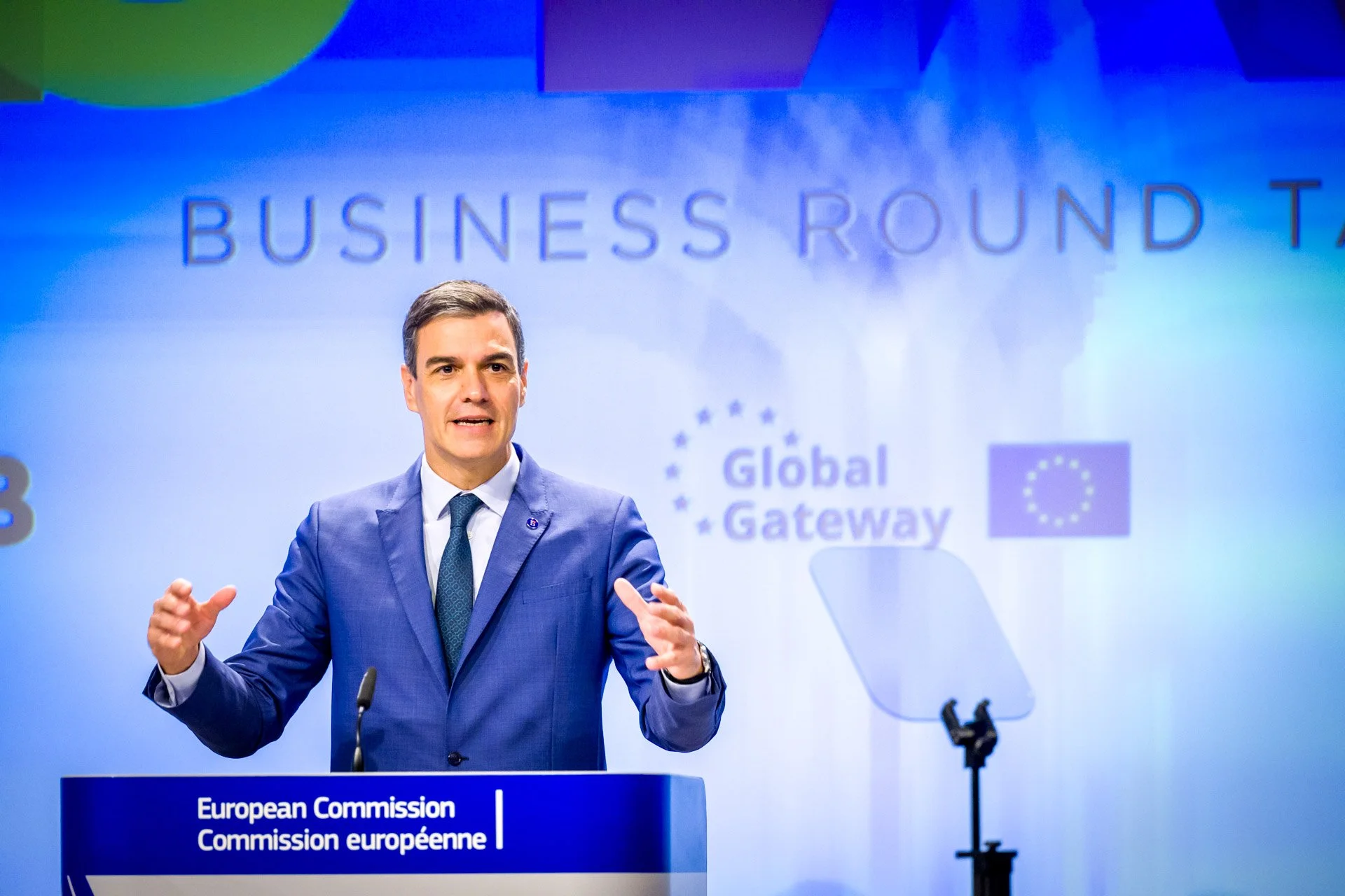 Un homme en costume bleu parle lors d'une conférence de presse avec un fond affichant 'BUSINESS ROUND TABLE' et des logos de l'Union européenne et 'Global Gateway'.