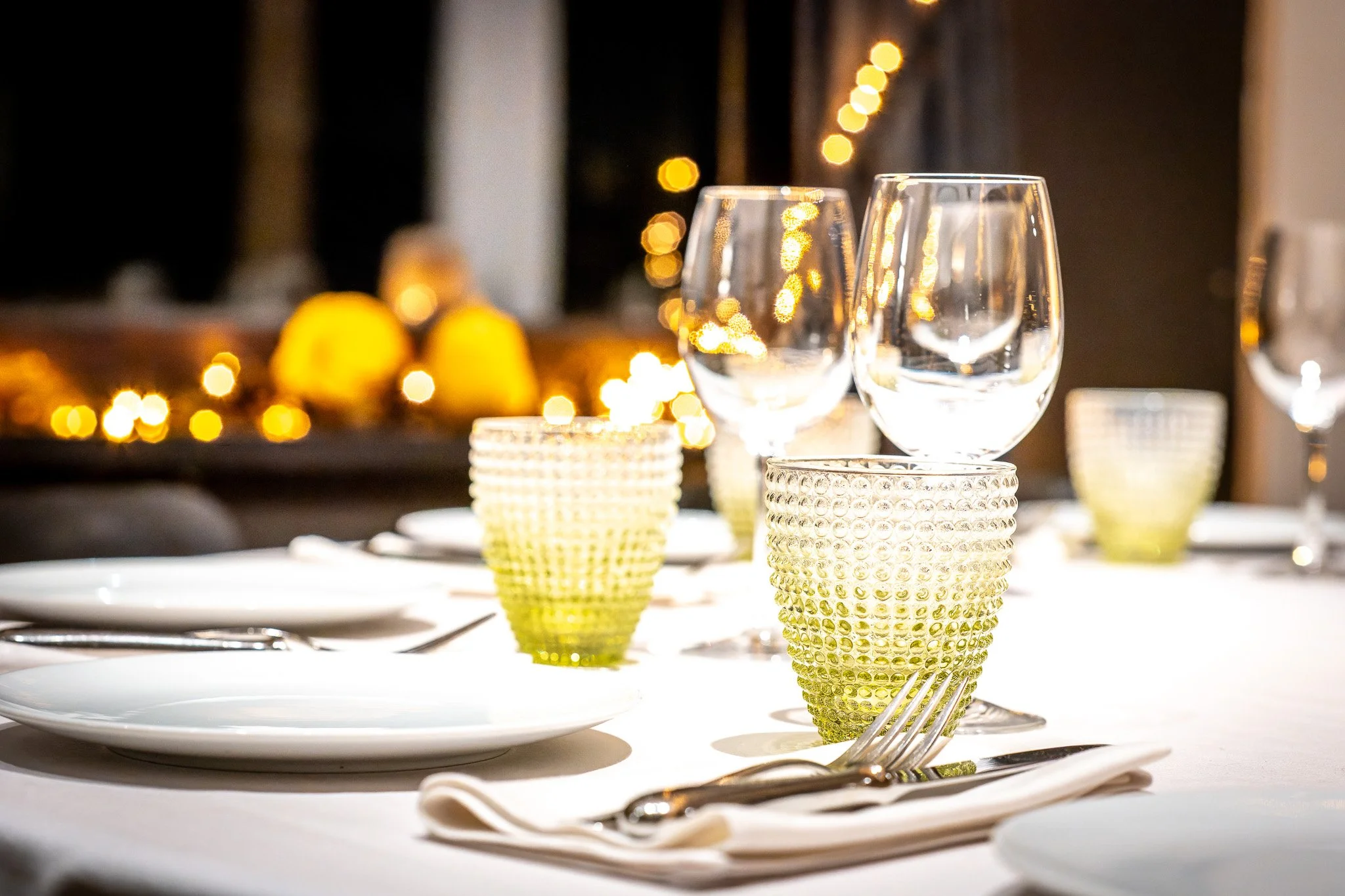 un événement d'entreprise. Table de dîner élégante avec verres à vin, assiettes et verres texturés, lumières d'ambiance en arrière-plan.
